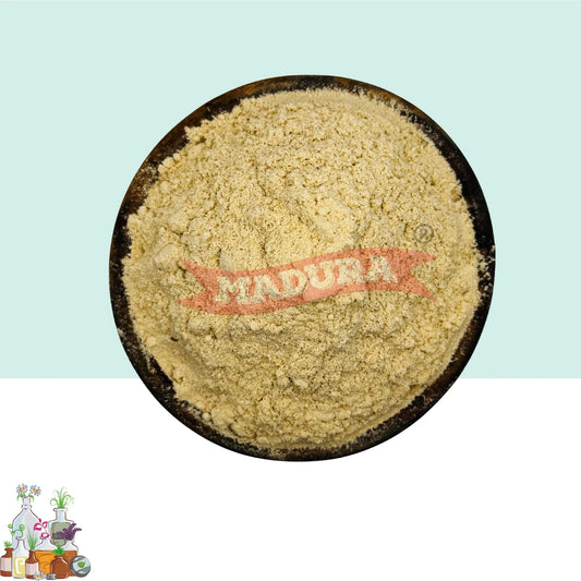 A top-down view of a mound of pale beige powder, likely Amchoor Powder placed in a dark round bowl. The powder has a red watermark reading 'MADURA' across the center.