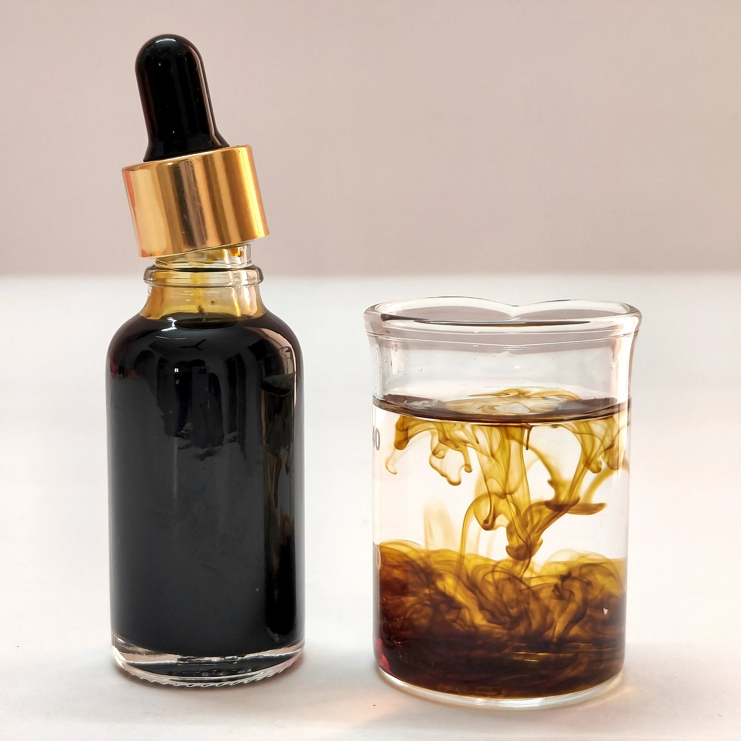Bottle of dark liquid with dropper next to a glass filled with the same liquid on a light background