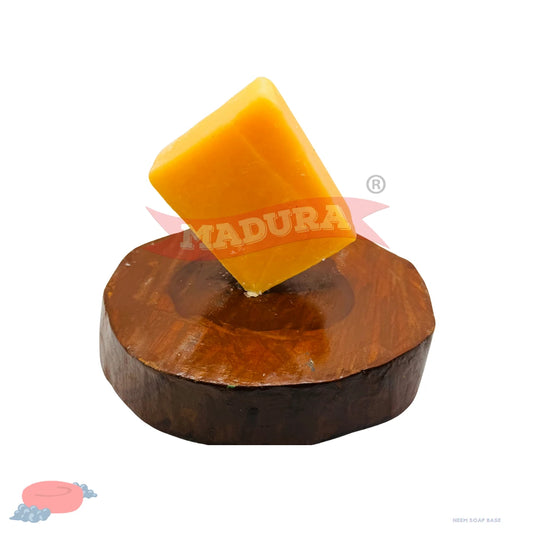 A rectangular bar of bright yellow soap standing upright on a round dark brown wooden slice, isolated on a white background with a red MADURA watermark across the center.