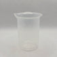 A translucent plastic measuring beaker with a pouring spout, featuring printed measurement markings in milliliters up to 50 ml, set against a light gray textured background.