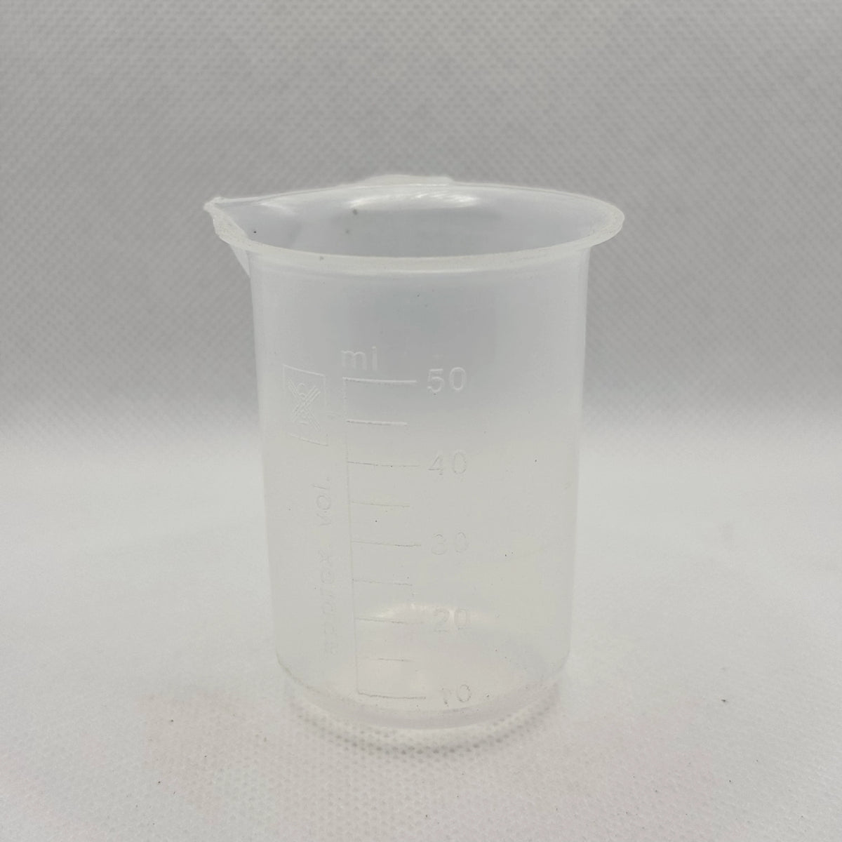 A translucent plastic measuring beaker with a pouring spout, featuring printed measurement markings in milliliters up to 50 ml, set against a light gray textured background.