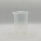 A small translucent plastic beaker with printed measurement markings in milliliters, shown against a light gray textured background.