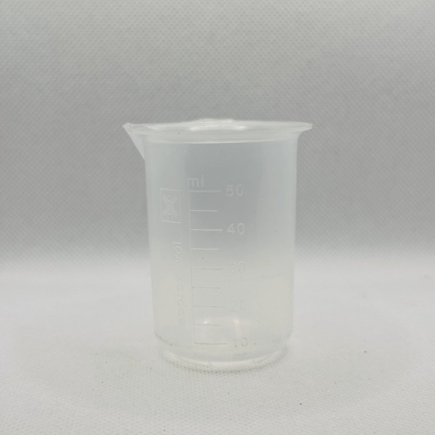 A small translucent plastic beaker with printed measurement markings in milliliters, shown against a light gray textured background.