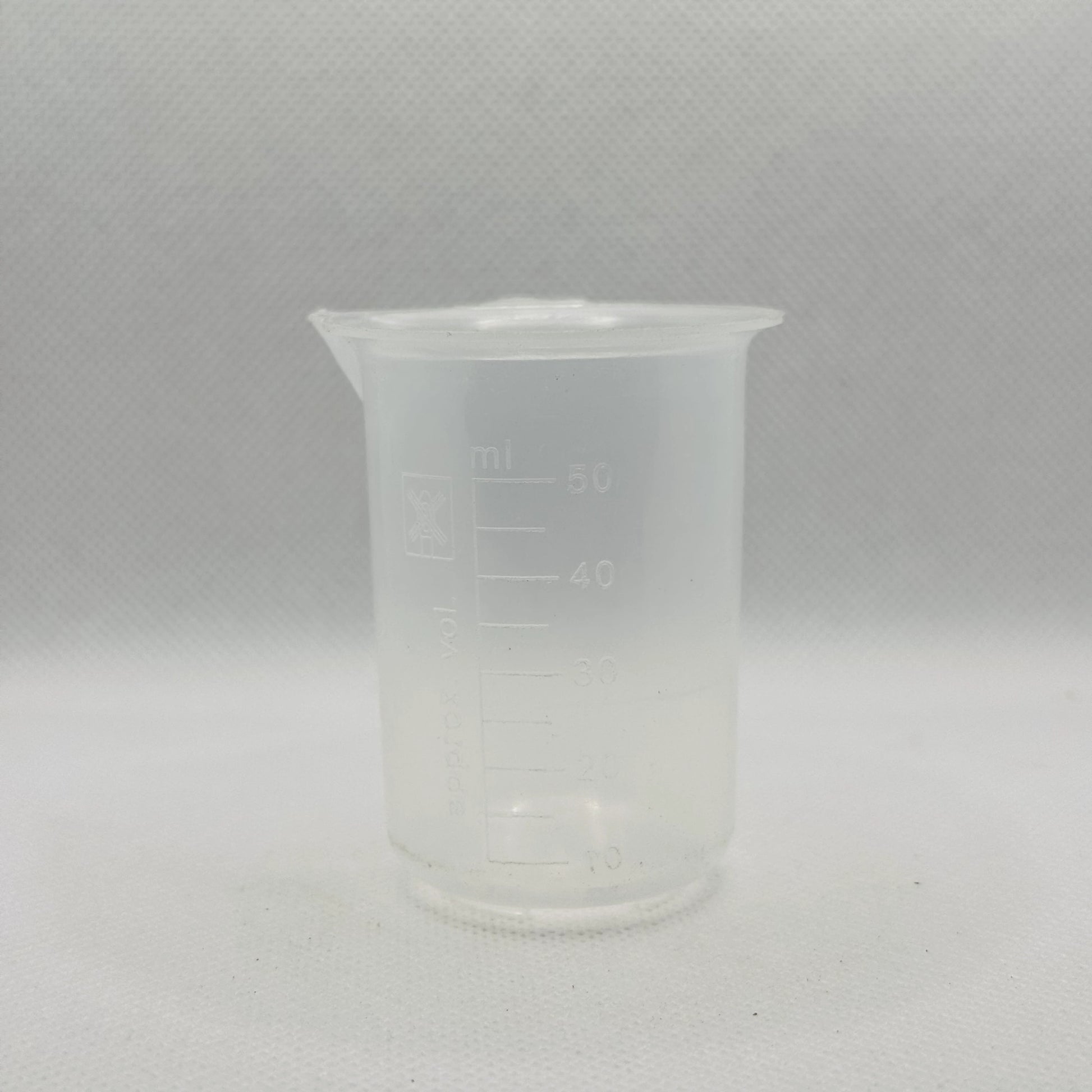 A small translucent plastic beaker with printed measurement markings in milliliters, shown against a light gray textured background.