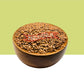 A wooden bowl filled with brown Wooden Flax Seed, centered against a split background with a light olive-green upper half and white lower half.