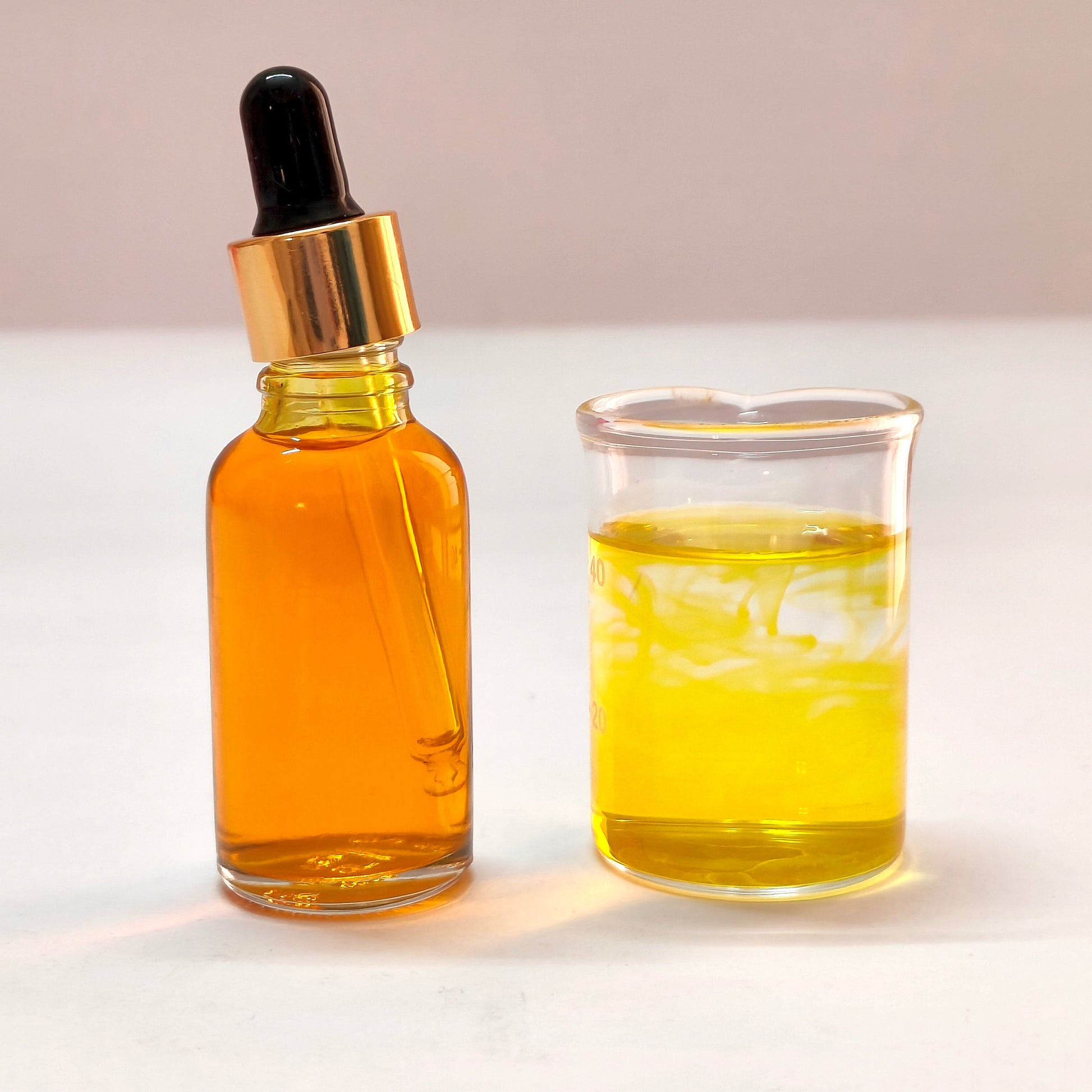 Glass dropper bottle and beaker filled with yellow liquid on a white background
