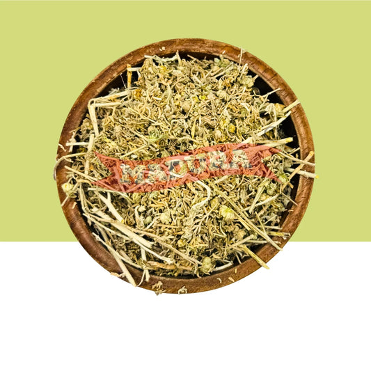 A round wooden bowl filled with dried herbal Marikolunthu, featuring pale green and beige botanicals with a prominent pinkish-red strip across the center, set against a split light green and white background.