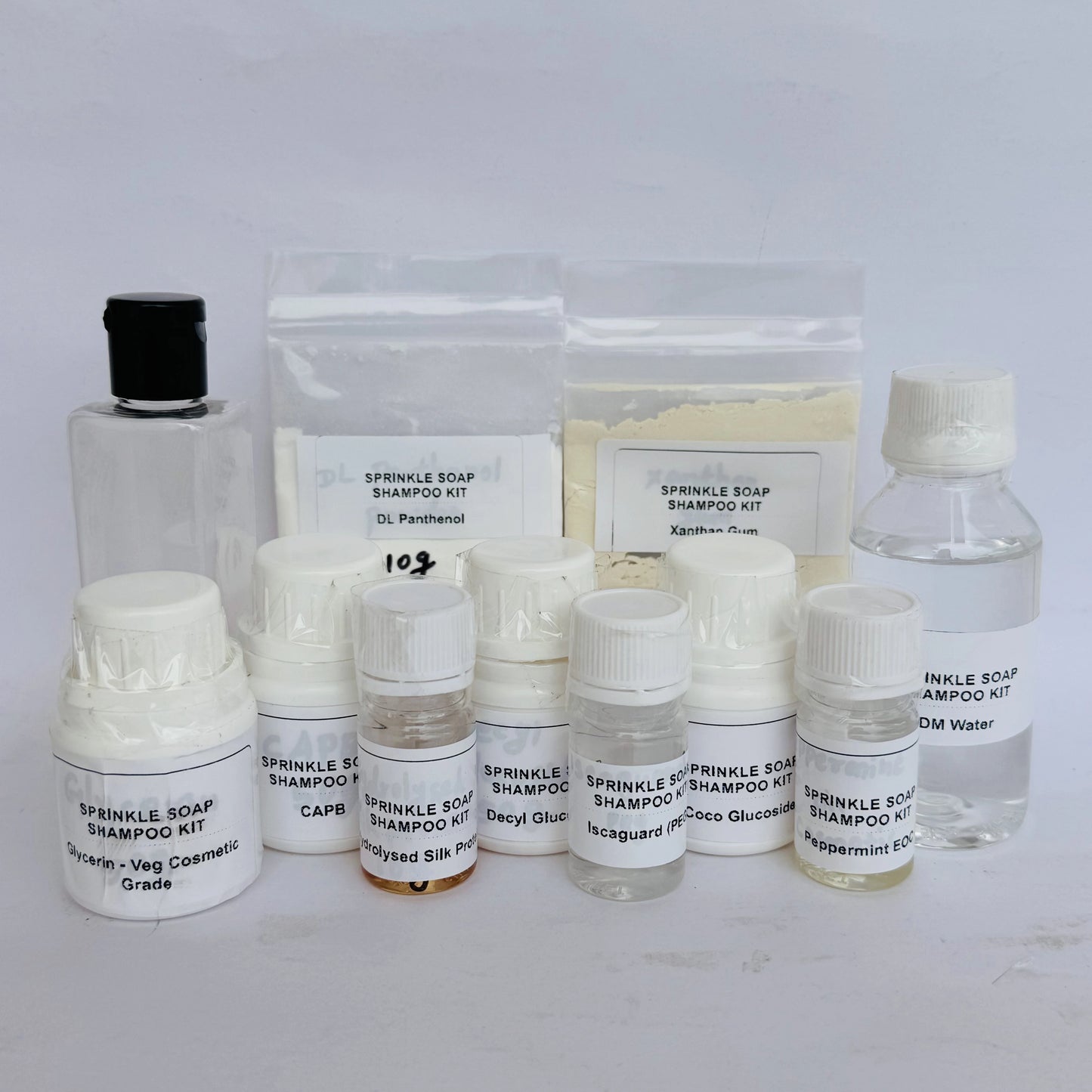 A skincare shampoo kit with multiple small bottles, jars, and pouches of ingredients arranged on a white surface against a white background. The labels read 'SPRINKLE SOAP SHAMPOO KIT' and include items such as capsaicin, deryl glucoside, triglyceride, peppermint oil, and water.